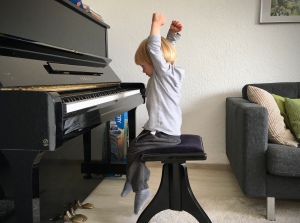 Kleinkind, das expressiv mit erhobenen Armen und wehendem Haar Klavier spielt. 