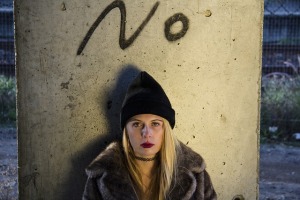 Ernst blickende junge Frau. Hinter ihr Graffiti: „No“