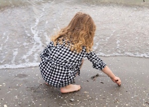 Mädchen am Strand von hinten, das Muscheln sammelt.